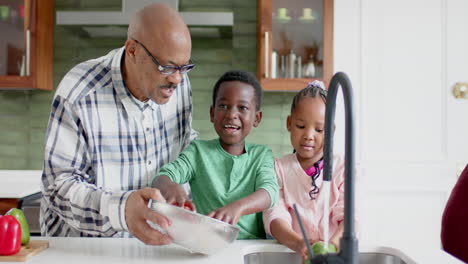 Glückliche-Afroamerikanische-Großeltern-Und-Enkelkinder-Beim-Gemüsewaschen-In-Der-Küche,-Zeitlupe