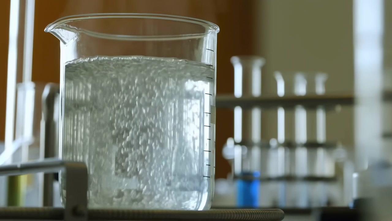 Primo piano di un becher che bolle su un banco da laboratorio, soluzione limpida che frigge vigorosamente in un becher di vetro riscaldato.