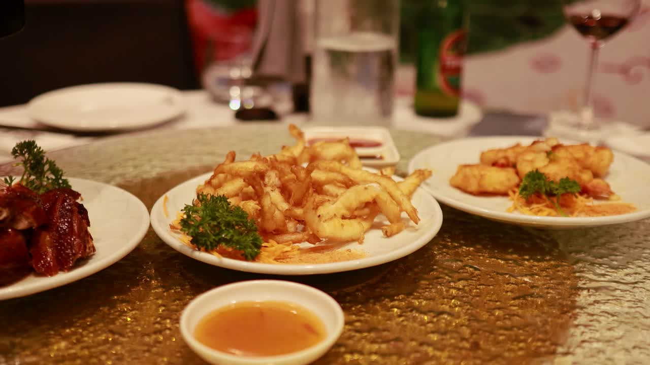 A rotating table displays Chinese dishes, sauces, and chopsticks in a restaurant setting with warm lighting