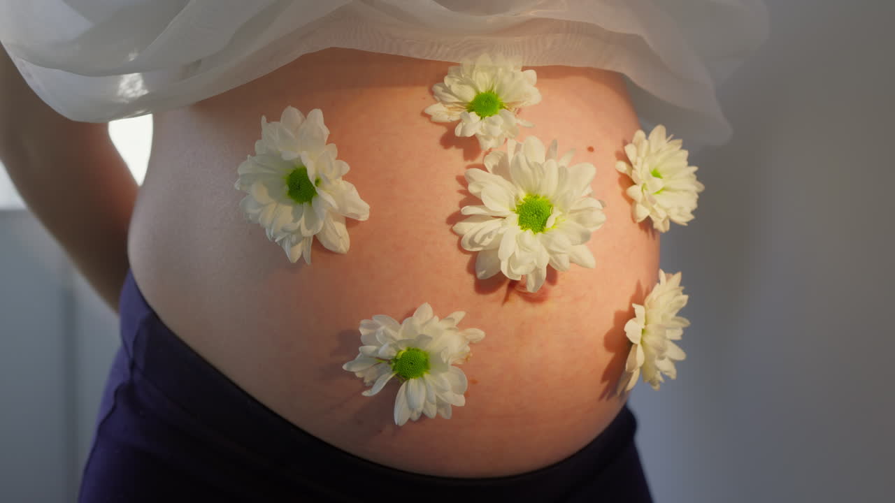 Primo piano della pancia di donna incinta adornata con fiori bianchi