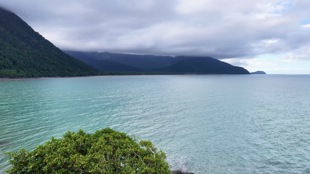 Lush greenery and rocky shores meet turquoise waters under a cloudy sky, showcasing the tranquil beauty of Thornton Beach