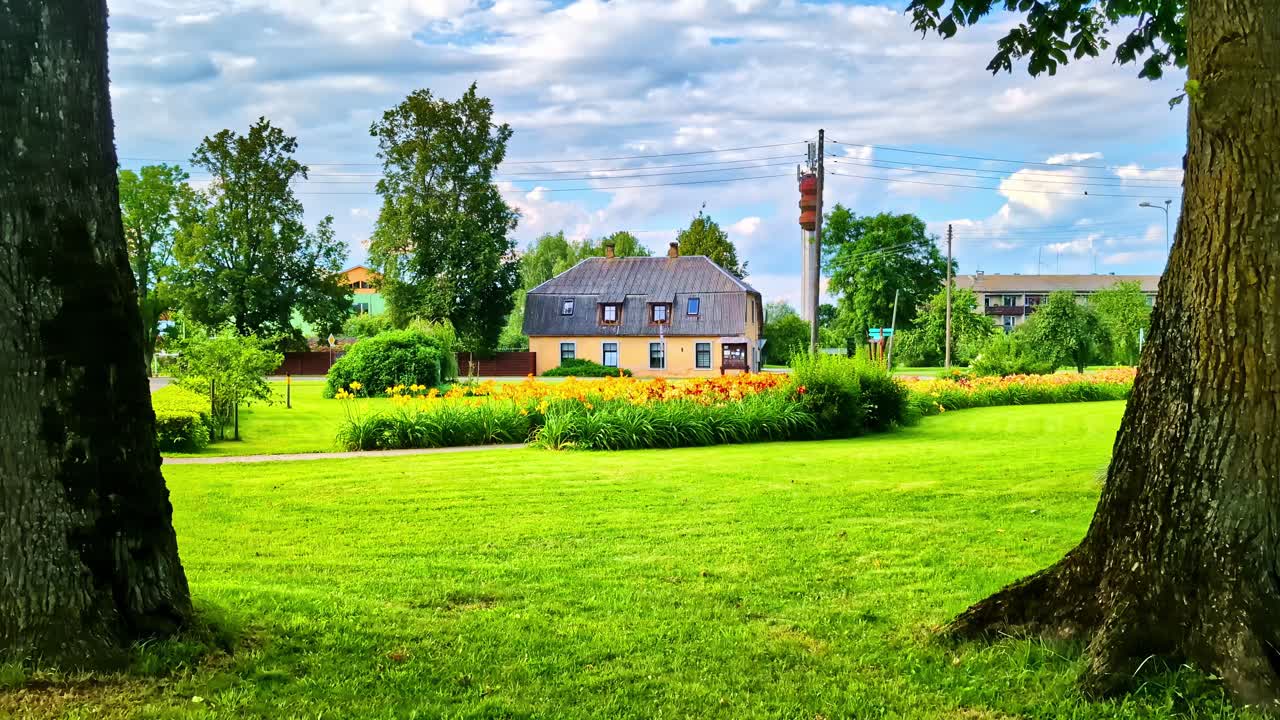 Lush green park lawn framed by tall trees with suburban house in background