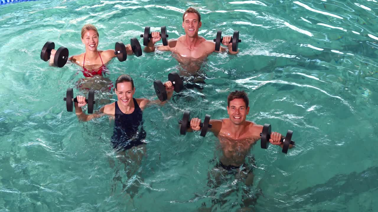 Fit people doing an aqua aerobics class in swimming pool with foam dumbbells