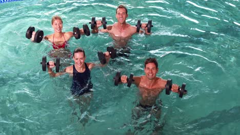 fit people doing an aqua aerobics class in swimming pool with foam dumbbells