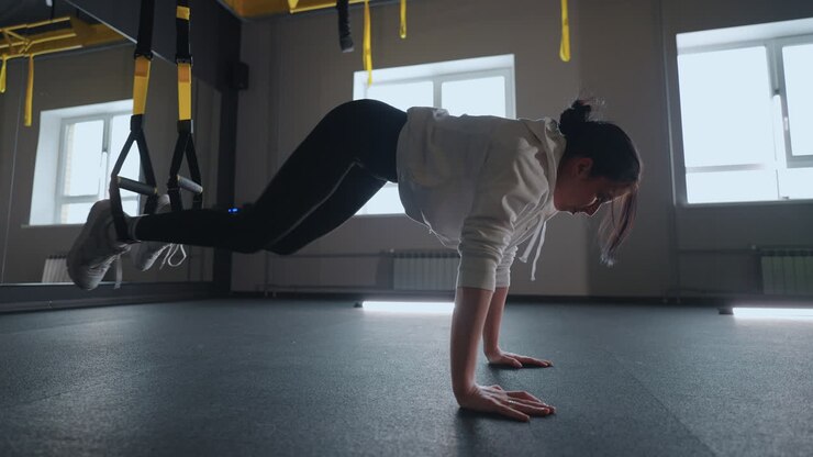 Doing TRX exercises. Young athletic woman in sports clothing training legs with trx fitness straps in the gym. exercise where stabilizing muscles trained and the whole body is working truly functional