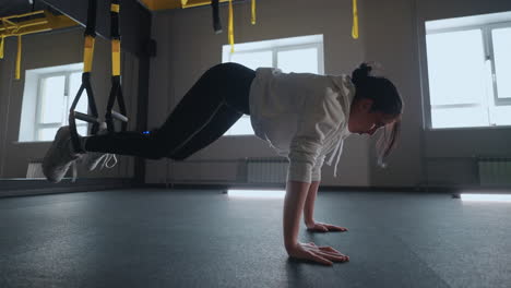 doing trx exercises. young athletic woman in sports clothing training legs with trx fitness straps in the gym. exercise where stabilizing muscles trained and the whole body is working truly functional