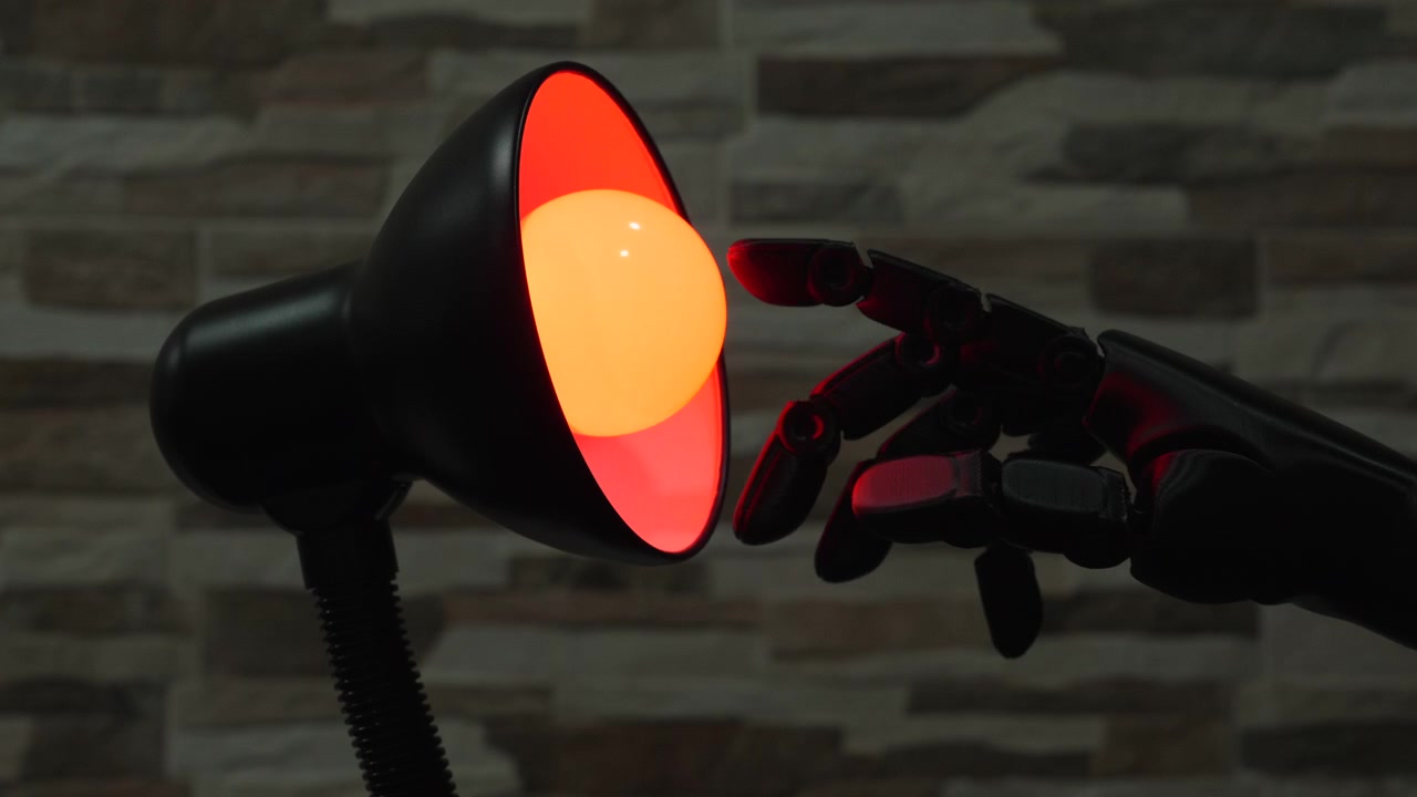 Svart robot- eller proteshand sträcker sig mot en glödande gul glödlampa i en modern skrivbordslampa mot en stenmur, användbar för koncept som AI, innovation och smart hem-teknik