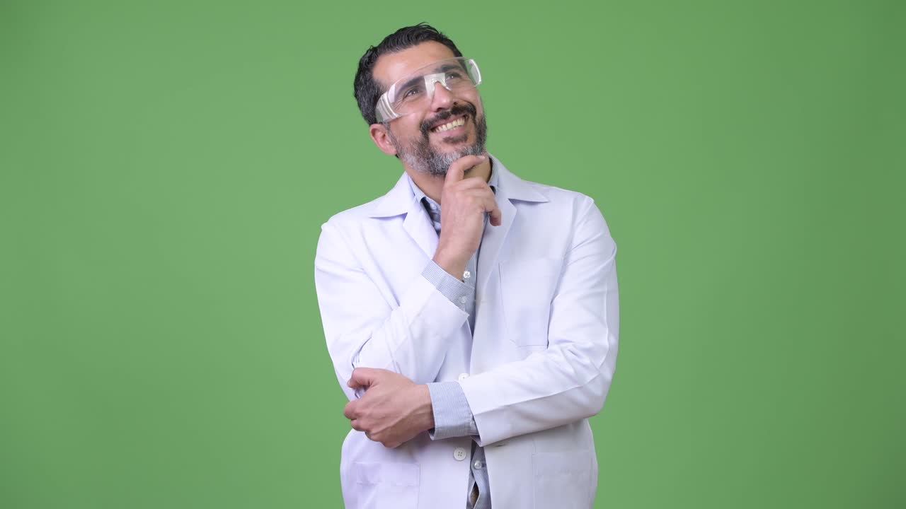 feliz persa hombre barbudo médico que lleva gafas de protección mientras piensa
