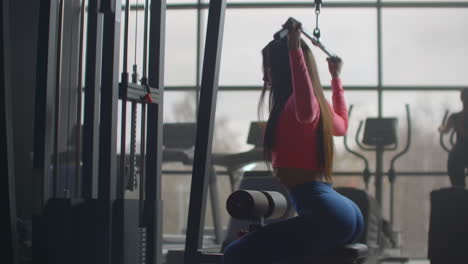 the young woman performs a personal training on the muscles of the back. she starts a barbell with a weight behind her back.