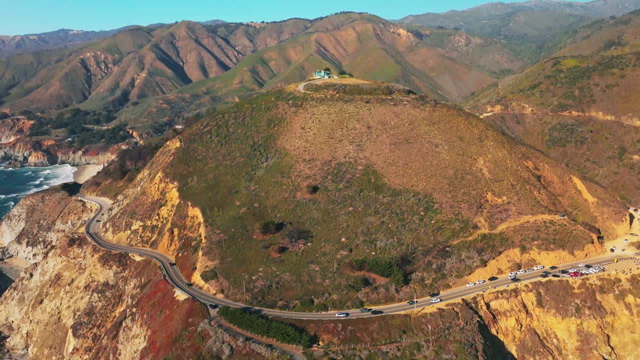 Approaching rounded mountain overgrown with moss with house on top. Busy road passing around the rock in the in the middle. Aerial view.