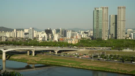 Tráfico-De-Automóviles-En-El-Puente-Eungbonggyo-Y-La-Autopista-De-Seúl-Y-El-Poro-De-Hanwha-Galleria,-Los-Rascacielos-Del-Bosque-Acro-De-Seúl-Desde-Un-Punto-De-Vista-Alto