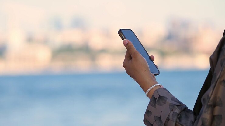 Donna con smartphone all'aperto e sfondo sfocato sul lungomare