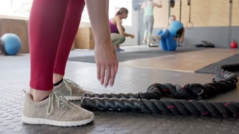 low section of unaltered biracial woman exercising with battling ropes at gym, in slow motion