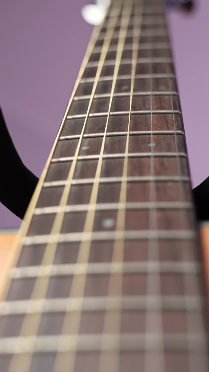 Vertical macro move up from the acoustic guitar bridge past the strings toward the fretboard and sound hole, showcasing wood grain and string vibration detail for music b-roll
