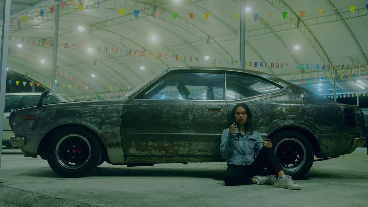 Woman Sitting Beside a Rusty Vintage Car at Night