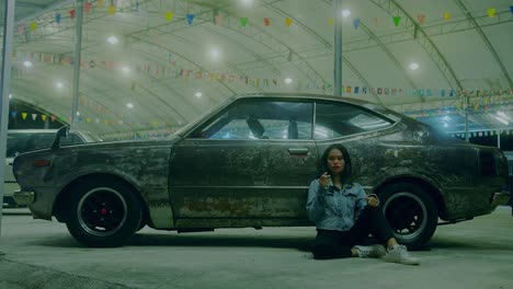 woman sitting beside a rusty vintage car at night