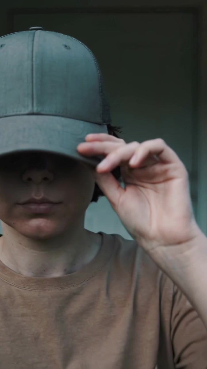 Vertical video: Stepping to entry, adult in brown tee, jeans pulling grey cap brim down hiding eyes