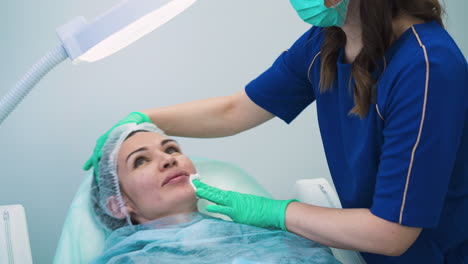 la esteticista con máscara pone un disco de algodón en la cara del cliente