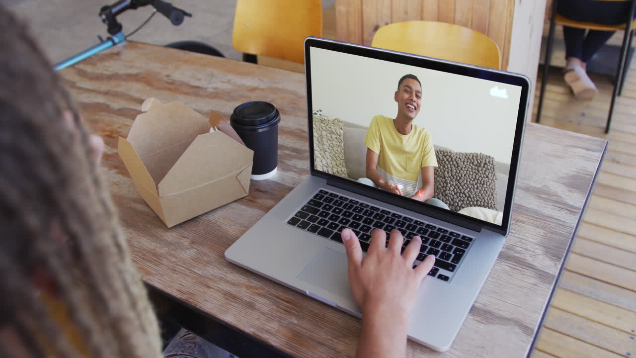 Woman having a snack while having a video call on laptop at cafe