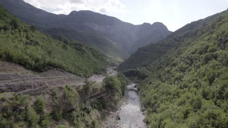 Drohnenvideo-Des-Aufsteigenden-Frontalflugzeugs,-Das-über-Das-Innere-Des-Cemi-Flusses-Auf-Der-Straße-Sh20-Zwischen-Den-Bergen-In-Albanien-Zwischen-Tamarë-Und-Selcë-Vorrückt,-Bewölkter-Himmel-Und-Türkisfarbenes-Flusswasser