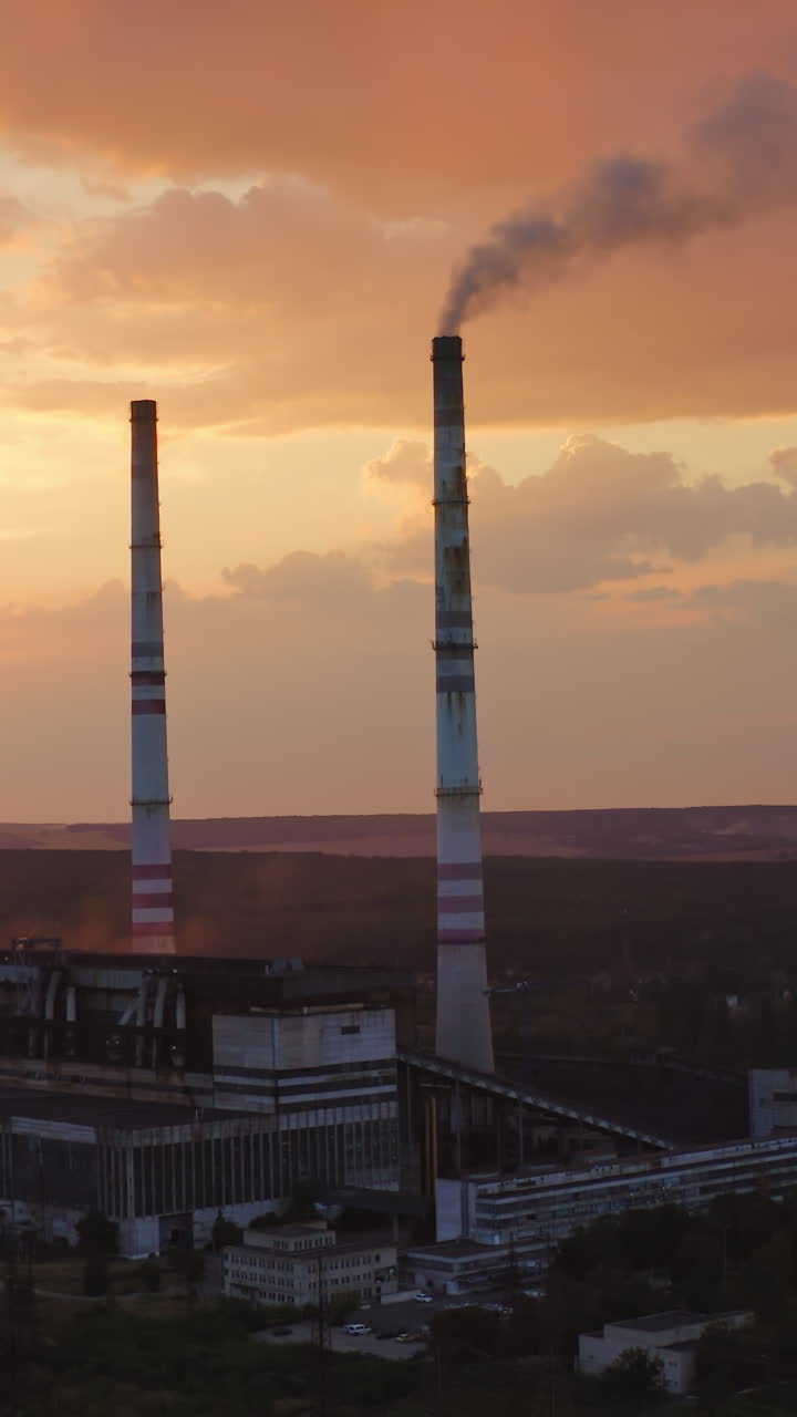 Harmful factory in the countryside. Industry with tower pipes on the evening sky with setting sun. Chemical smoke from manufacture pollutes the air. View from above. Vertical video