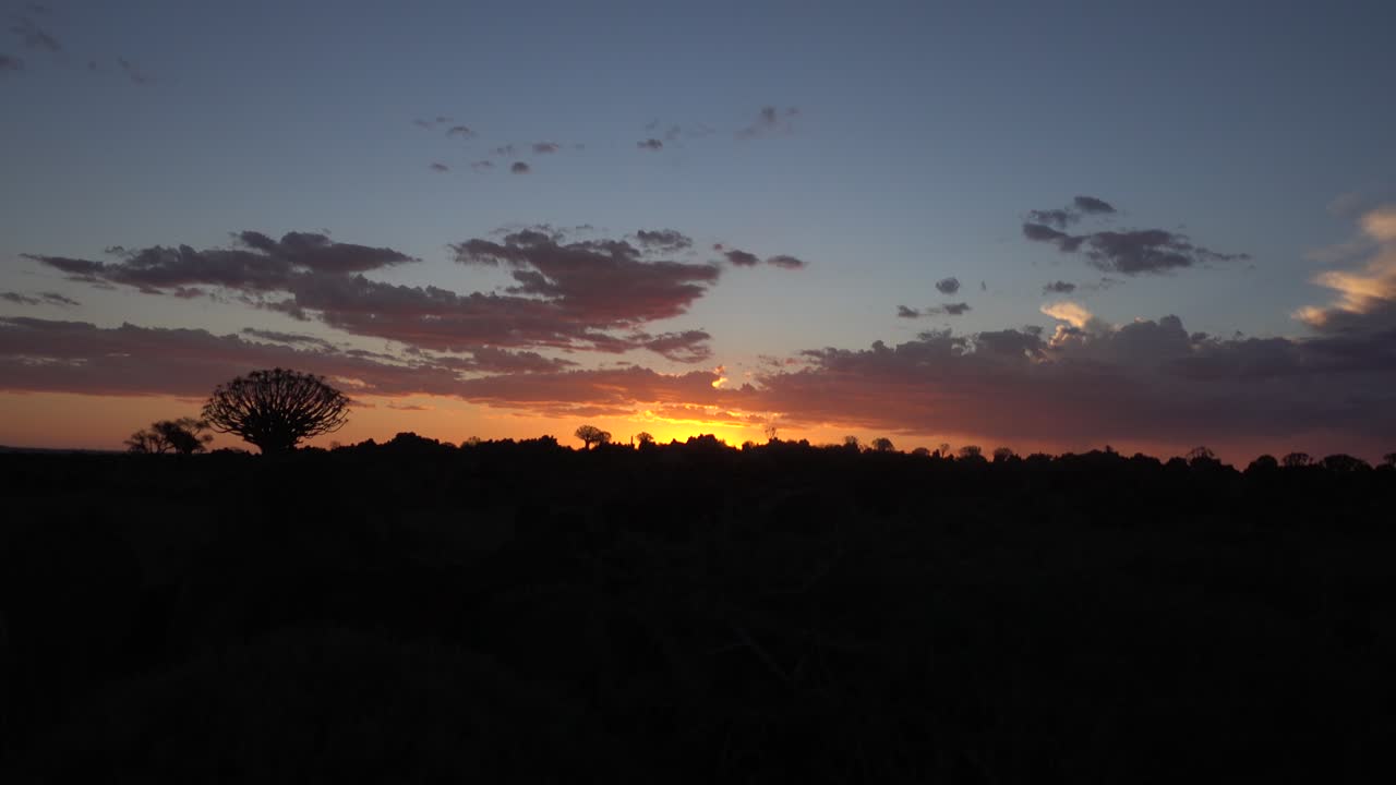 lapso de tiempo de la puesta de sol en namibia, áfrica, con nubes en movimiento y árboles de silueta en el fondo