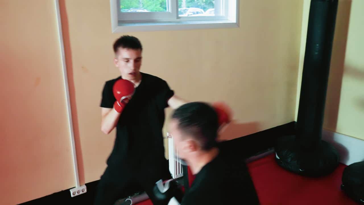 Fighters in boxing gym during sparring session, one athlete bending low protecting head while opponent punch, gloves raised, intense physical contact, endurance, strength, combat focus, martial practice