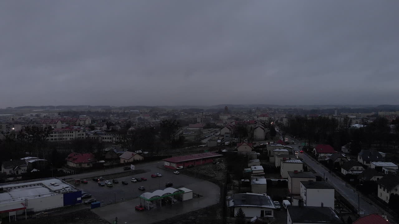 Smooth reverse flight over a small town, cars are on the road, large car park and car wash nearby
