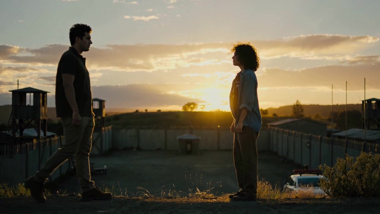 Entering man walking toward woman on berm at sunset, meeting by walled compound and watchtowers