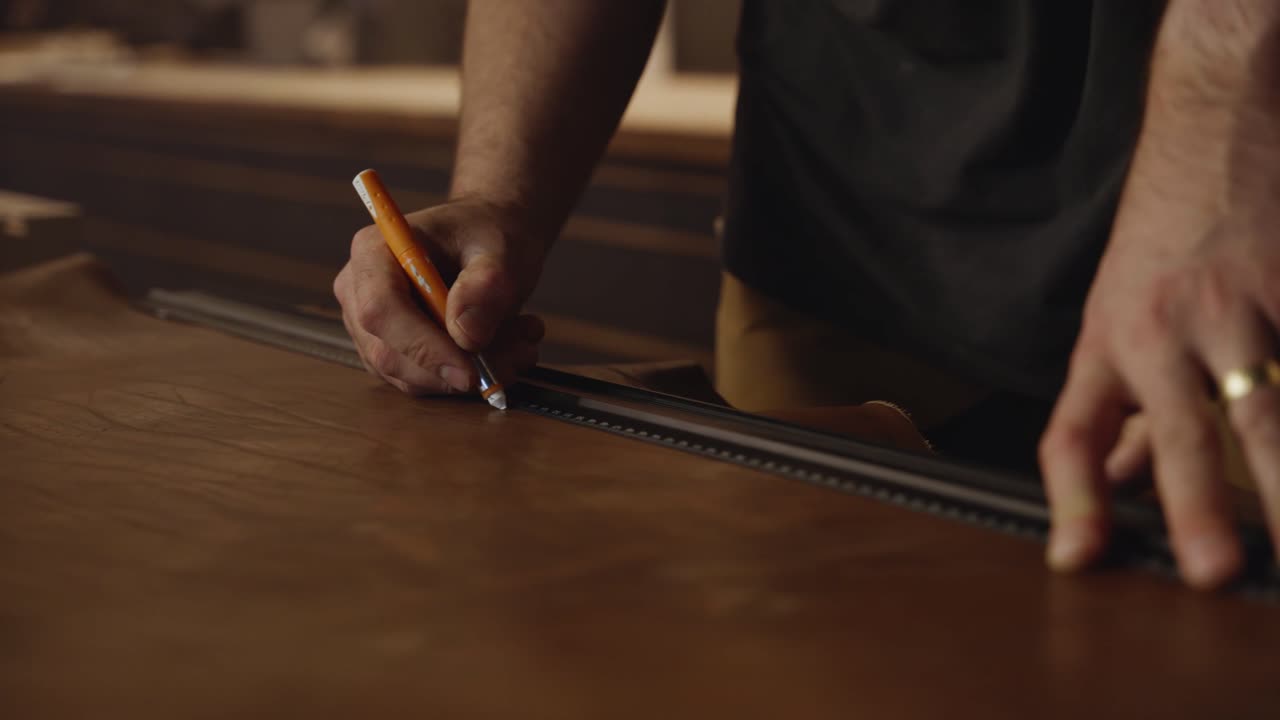 Close-up of an artisan carefully marking measurements on leather with a pencil and ruler in a workshop, showing precision, craftsmanship, and handmade design preparation