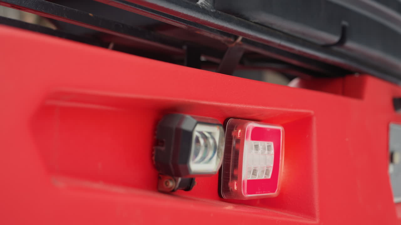 ATV rosso, primo piano dei fari del paraurti anteriore che mostrano una lampada LED quadrata, catarifrangente rosso, supporto metallico, alloggiamento in plastica, bulloni di montaggio, fiocchi di neve, sporco, ispezione in officina, prontezza fuoristrada, robusto, avventura, durevole.