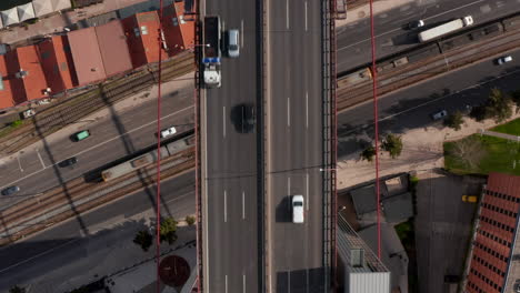 Aerial-birds-eye-overhead-top-down-view-of-traffic-on-highway-bridge-leading-over-street-and-railway-track.-Zooming-out-footage-from-drone.-Lisbon,-capital-of-Portugal.