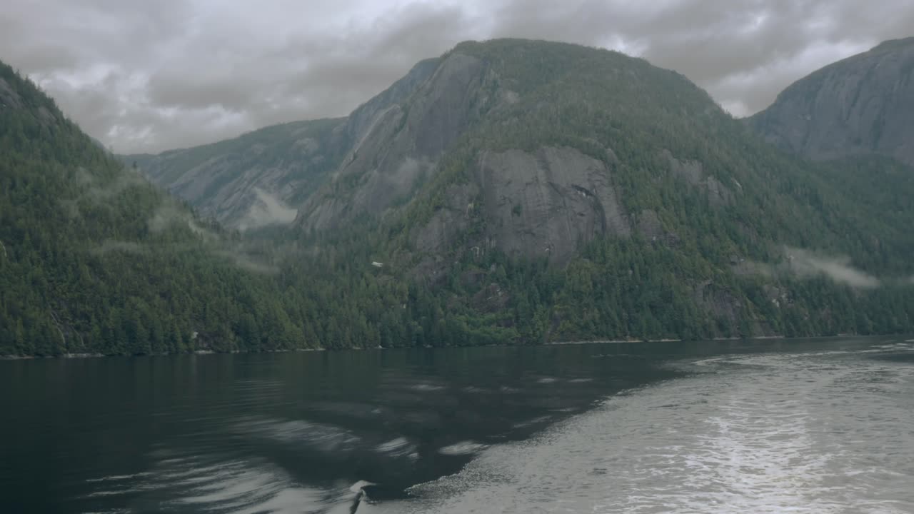 Un idrovolante vola, in lontananza, a bassa quota attraverso un fiordo dell'Alaska