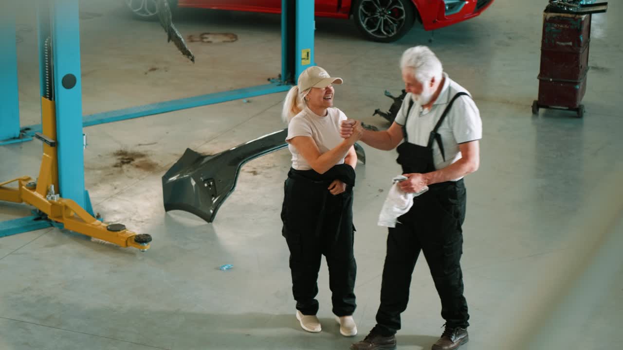 trabajadores mecánicos satisfechos haciendo el gesto de los cinco altos y hablando después de terminar el trabajo en el garaje