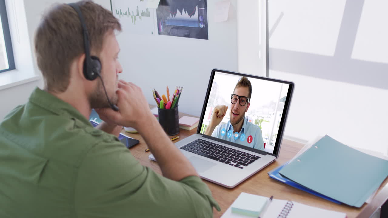 Kaukasisk mand bruger bærbar computer og telefonheadset på videoopkald med en mandlig kollega.