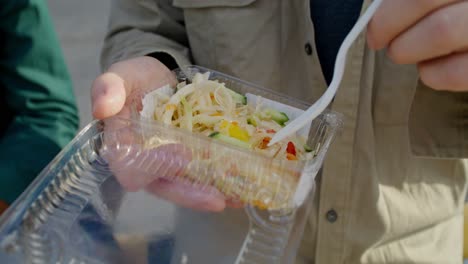 persona comiendo una ensalada de un recipiente para llevar