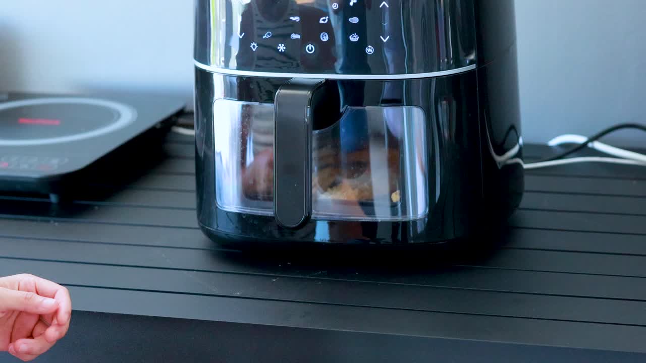 Una persona attiva una friggitrice ad aria digitale su un bancone della cucina, premendo il pulsante di accensione con un gesto di pollice in su in una luce brillante e naturale.
