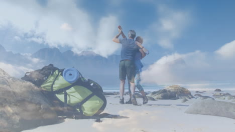 pareja de ancianos caucásicos haciendo senderismo bailando junto al mar, sobre nubes que se mueven rápidamente