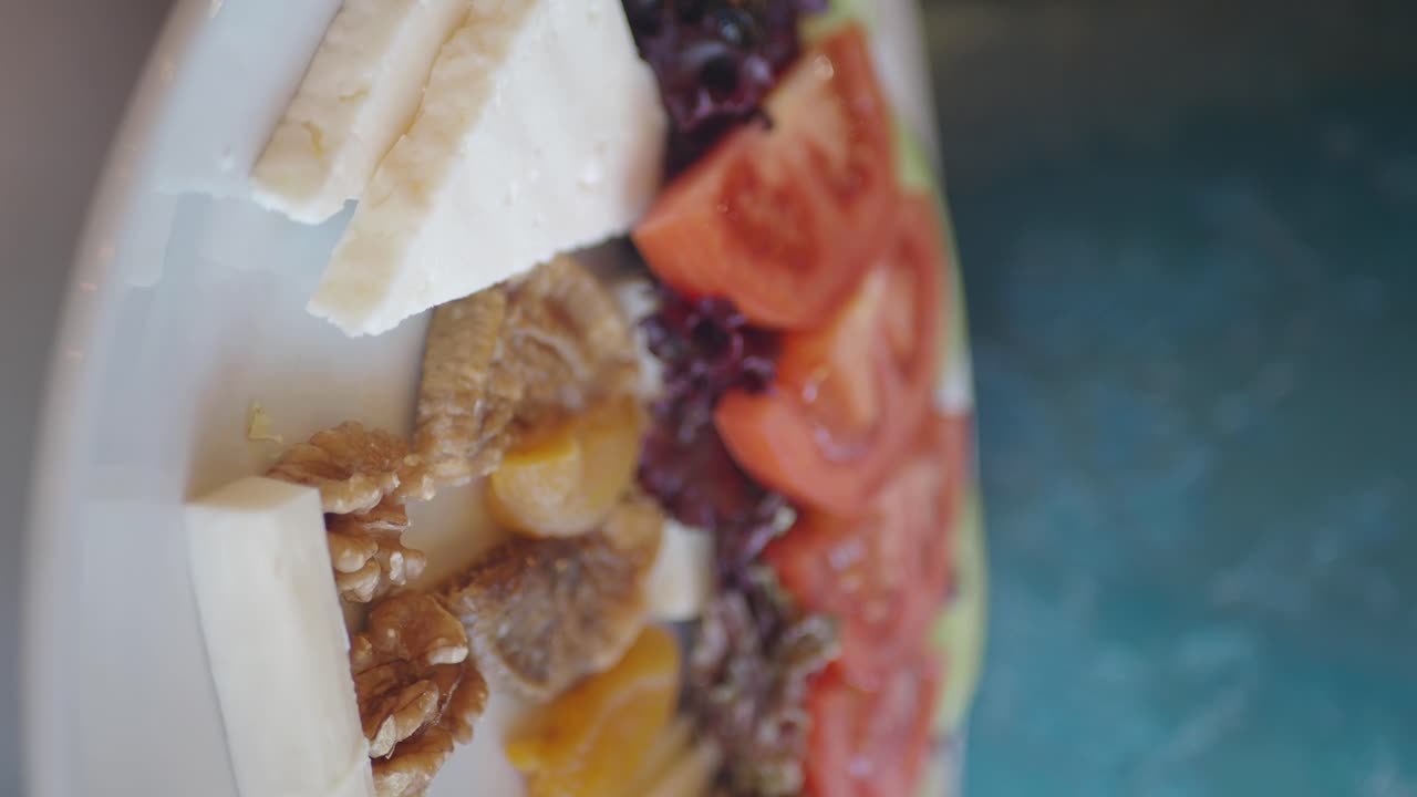 Close-up of a food platter with cheese, walnuts, dried fruits, tomatoes, and lettuce