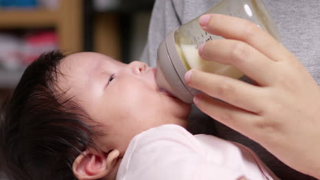 the hungry newborn infant is sucking some milk from a baby bottle that is being held by her mother and she is cradling her in her arms