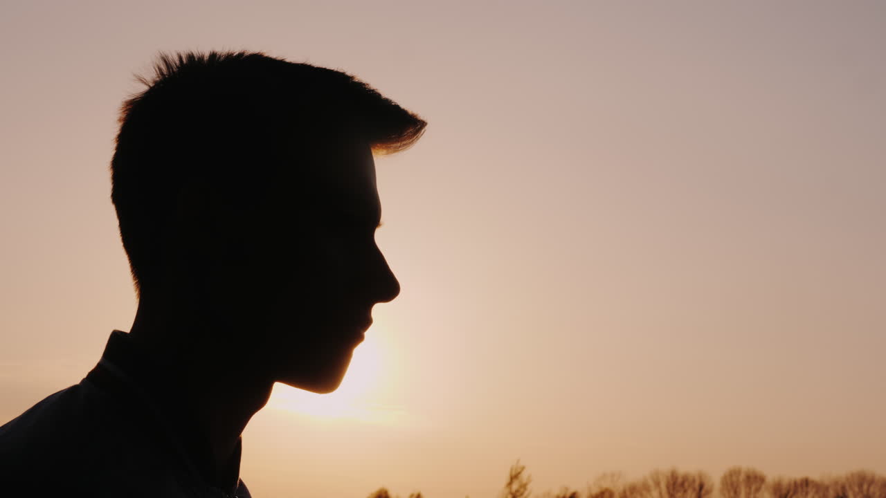 Profilo di un adolescente che mangia snack. Silhouette contro il sole al tramonto.