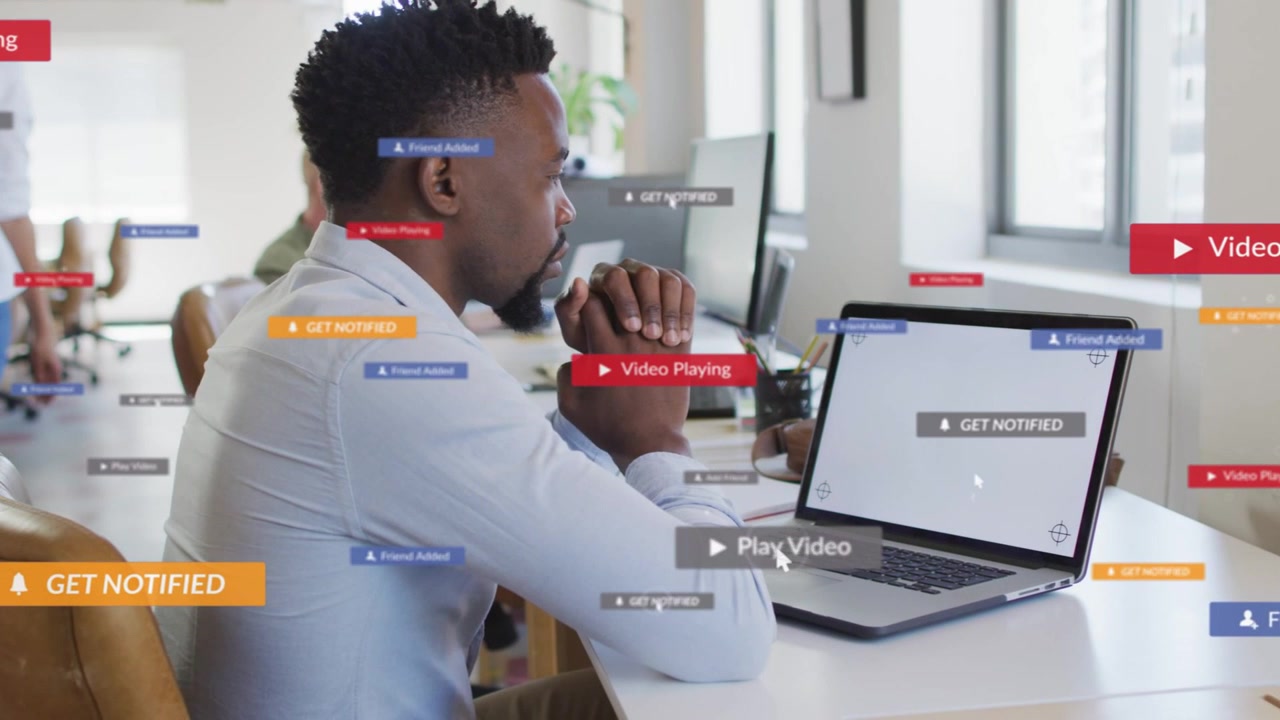 Man on laptop at desk alerts coming floating UI labels around him cluttering business then clearing