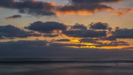 asombroso y hermoso timelapse dorado de la puesta de sol con rayos de luz que se transmiten a través de espesas nubes sobre las tranquilas olas del océano que fluyen