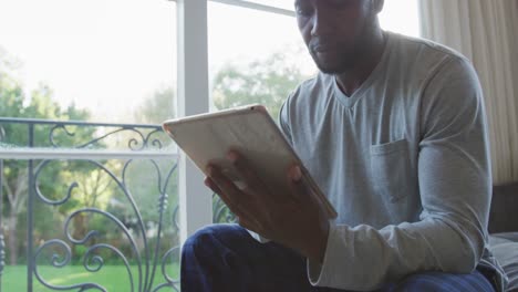 Afroamerikanischer-Mann-Nutzt-Digitales-Tablet,-Während-Er-Zu-Hause-Auf-Der-Couch-Sitzt
