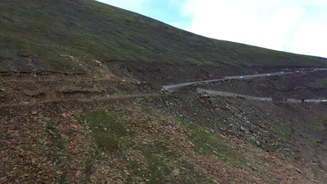 Drone-shot-of-a-Tuk-Tuk-on-Babusar-pass-in-Pakistan,-with-a-few-vehicles-on-the-road-below-in-the-Kaghan-Valley,-wide-revealing-shot