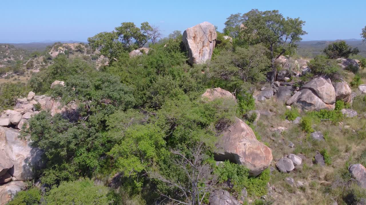 vista de avión no tripulado sobre una colina rocosa y arbustiva para revelar una llanura africana con una carretera sinuosa