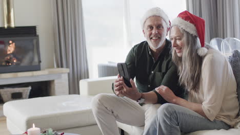 Pareja-Caucásica-De-Mediana-Edad-Con-Sombreros-De-Santa-En-Video-Chat-De-Tableta-En-Navidad-En-Casa,-Cámara-Lenta