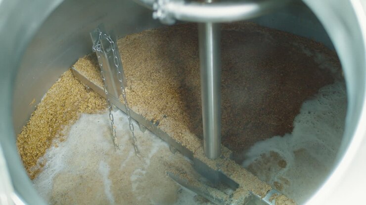Fabbrica di produzione di birra artigianale, birrificio. Primo piano di grani di malto d'orzo. Birrificazione, produzione di alcol in tini di metallo e imbottigliamento.