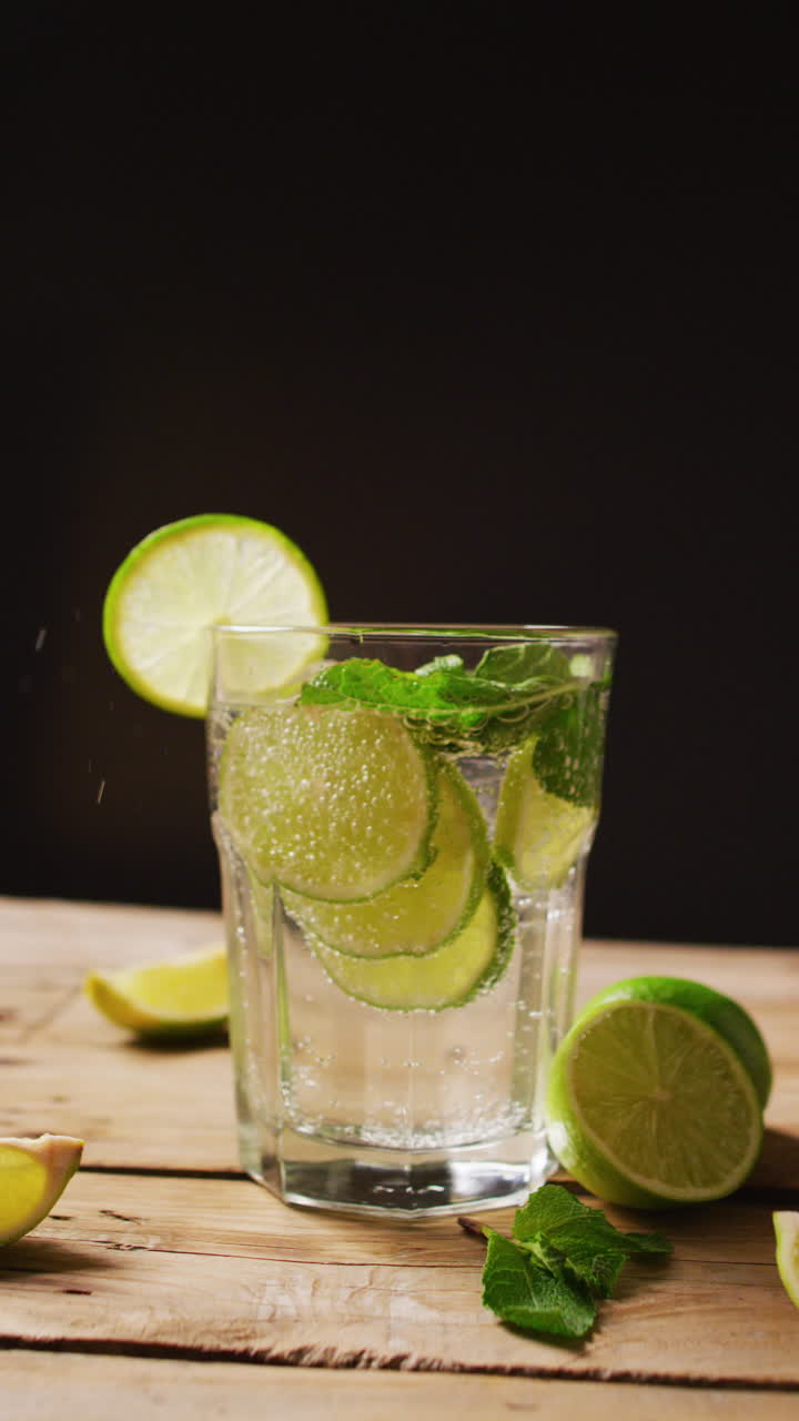 Vertical video of close up of drink with limes on black background, with copy space