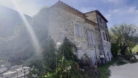 Pequeña-Y-Antigua-Granja-De-Piedra-En-Francia-Bajo-El-Sol-Con-Ventanas-Antiguas-Cubiertas-Por-La-Naturaleza-Con-Un-Sendero-Delante